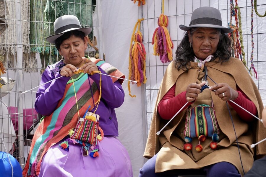 Tejedora con vestimenta tradicional andina hilando en la plaza